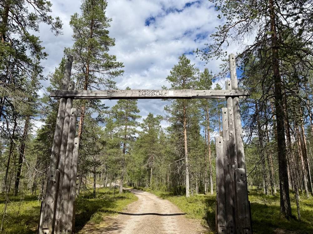 Großes hölzernes Eingangstor mit der Aufschrift Korouoma Lapiosalmi über einem Waldweg