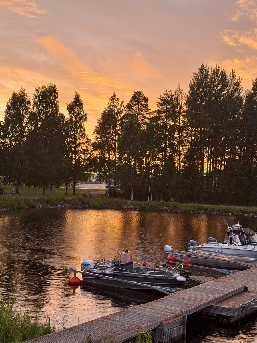 Sonnenuntergang mit orange leuchtenden Wolken über Bäumen, im Vordergrund Motorboote am Steg