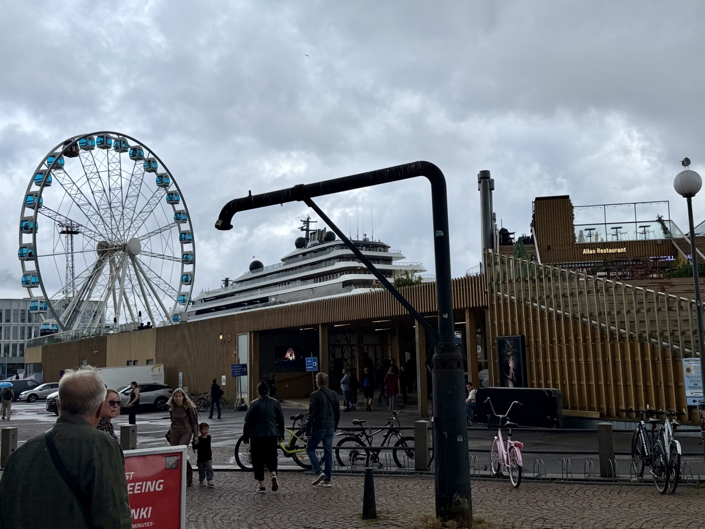 Riesenrad am Hafen von Helsinki vor grauem Himmel, dahinter ein großes Fährschiff