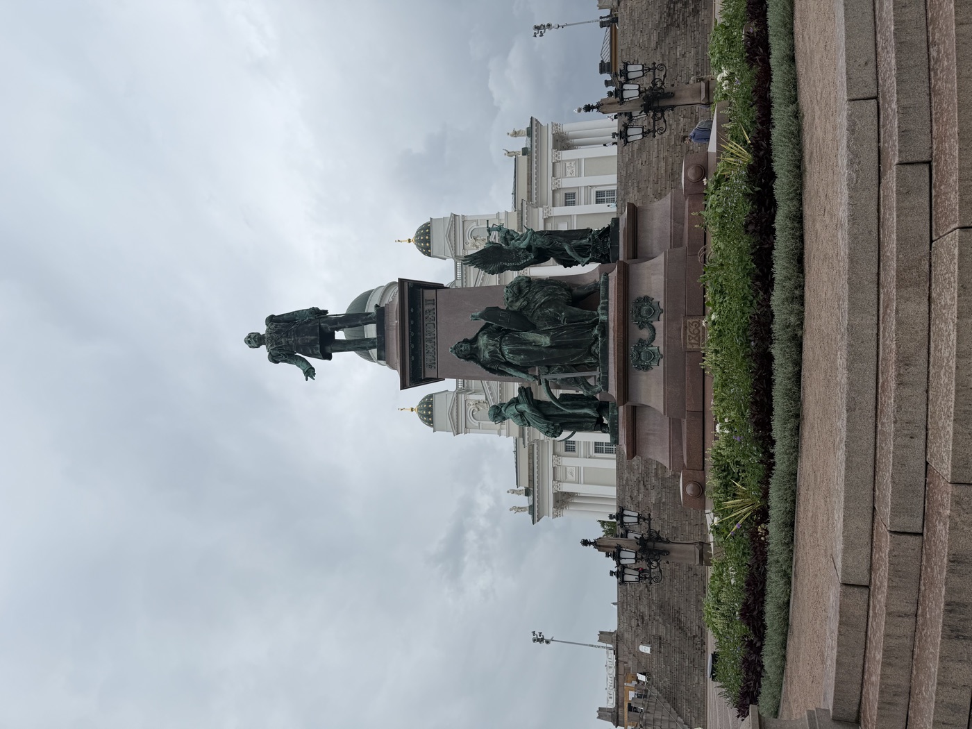 Bronzedenkmal auf einem Sockel vor dem Helsinkier Dom unter bewölktem Himmel