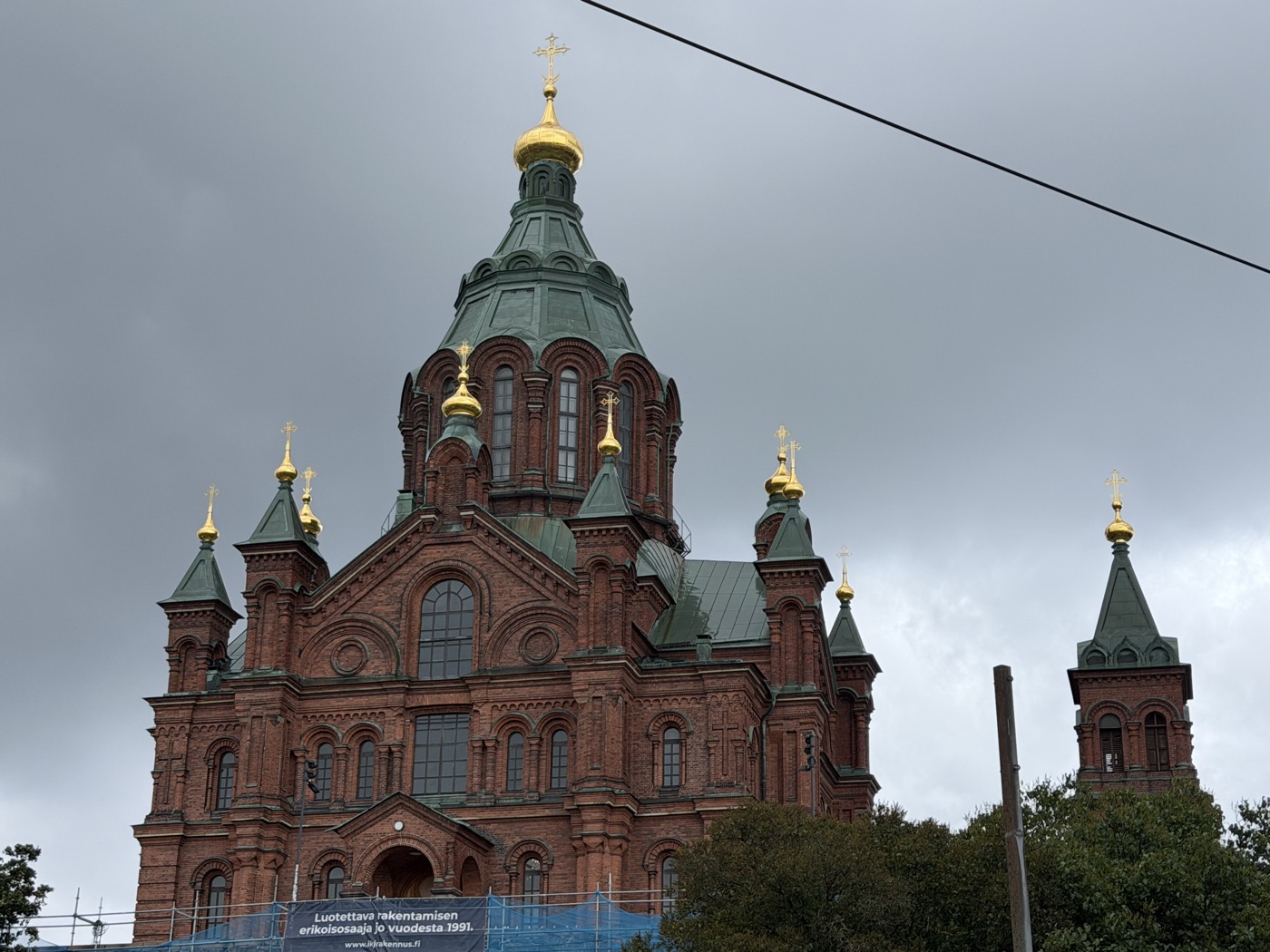 Rote Backsteinkirche mit grünen Dächern und goldenen Kuppeln vor dunklen Wolken