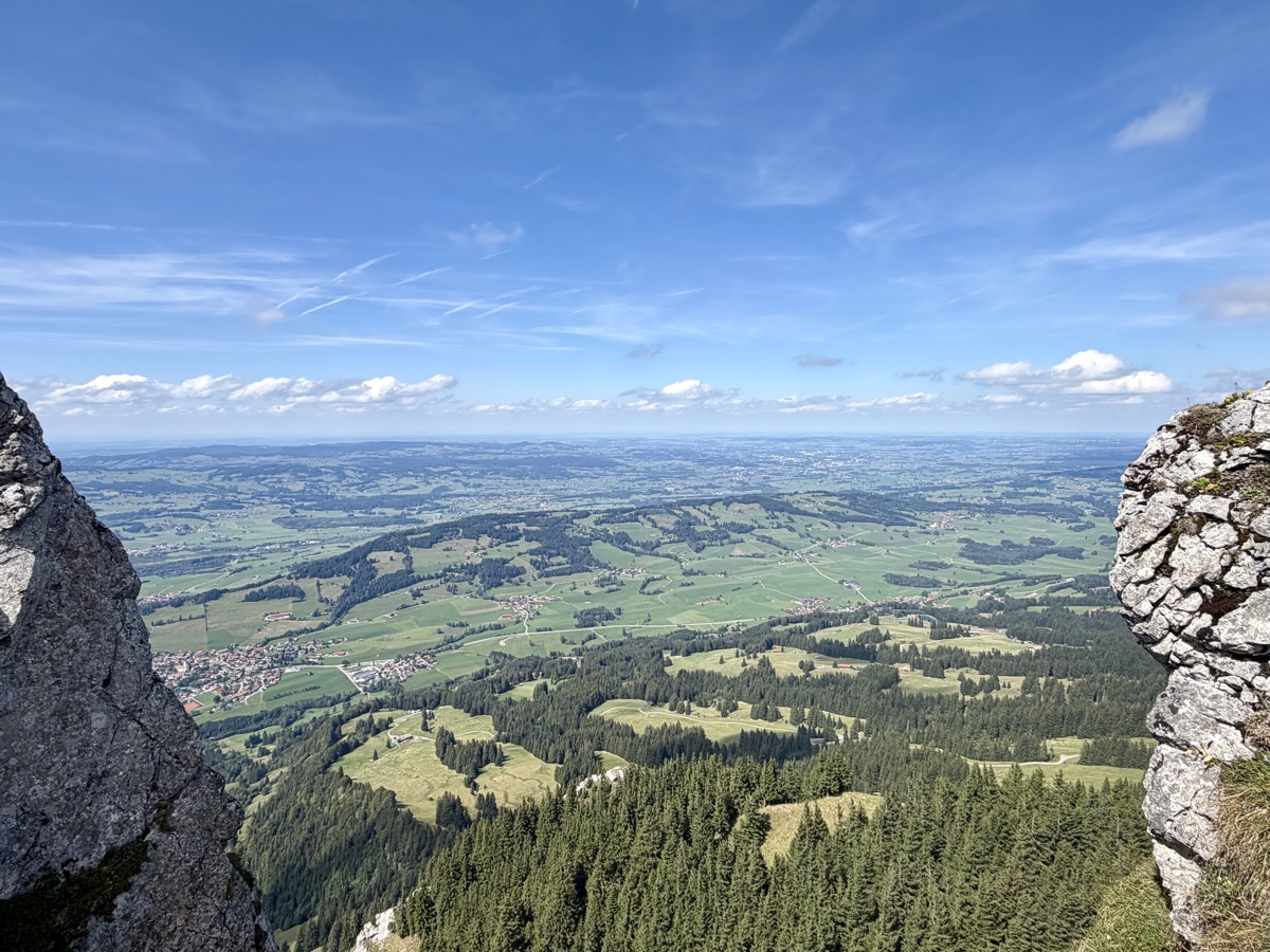 Blick zwischen zwei Felswänden hinunter auf Wiesen, Wälder und Dörfer im Allgäu