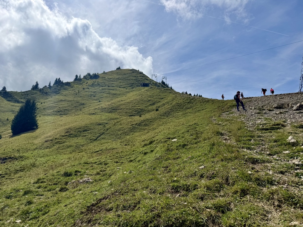 Steile Grasflanke mit einem Pfad, auf dem mehrere Wanderer aufsteigen