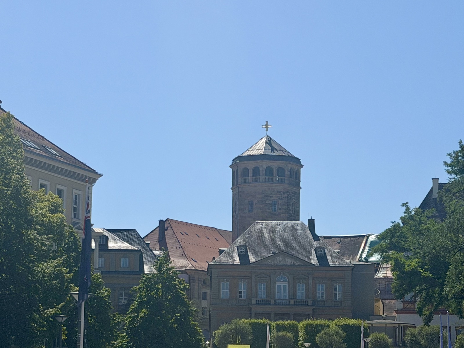 Turm mit Pyramidendach hinter Bäumen und historischen Gebäuden