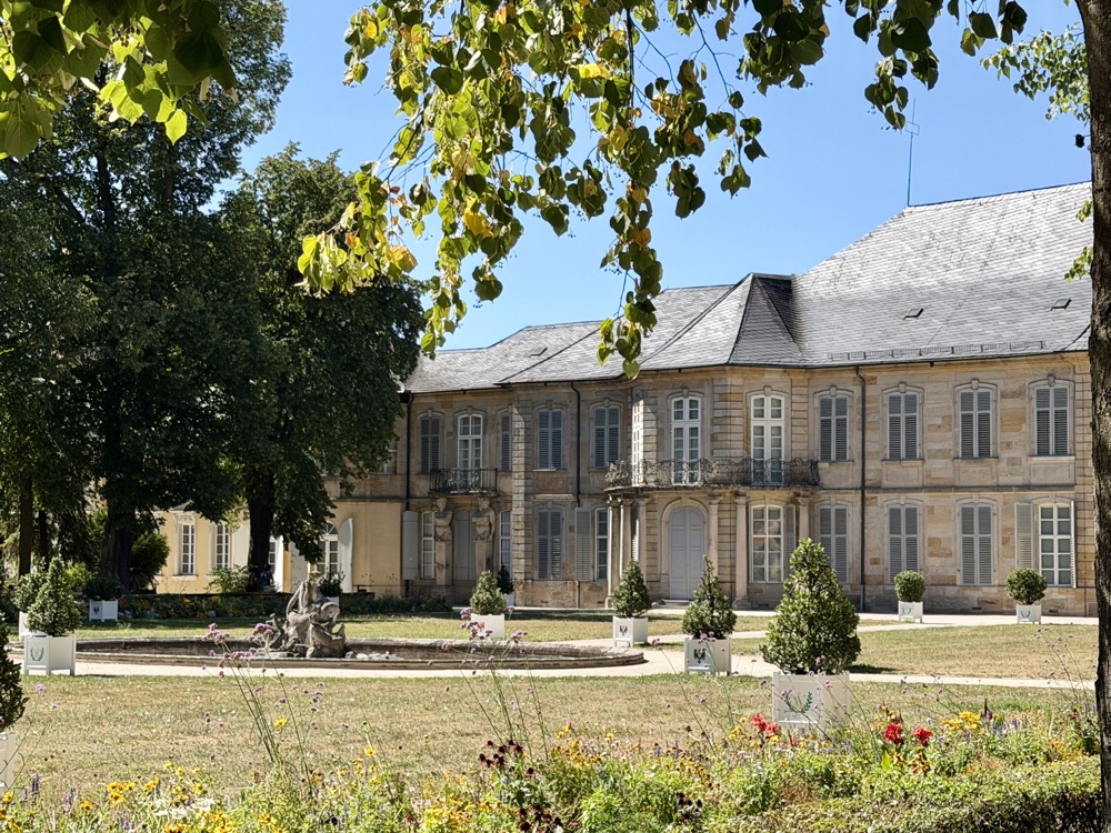 Schloss mit grauem Dach hinter gepflegten Beeten und Bäumen im Hofgarten