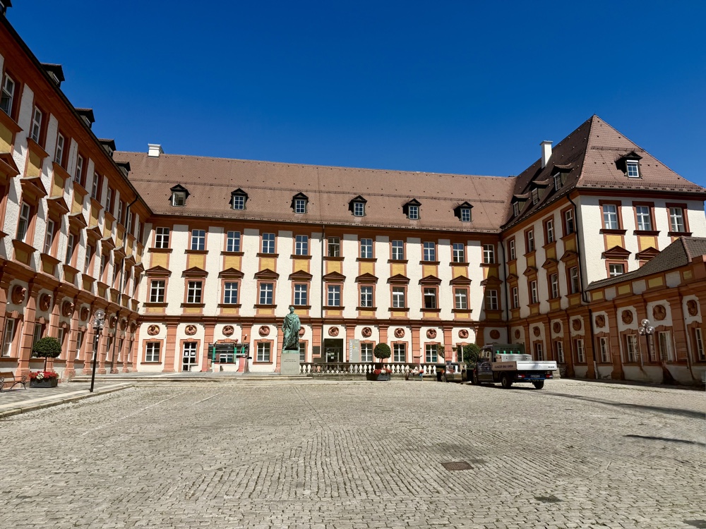 Hofansicht eines Schlosses mit gelber Fassade und roten Zierstreifen