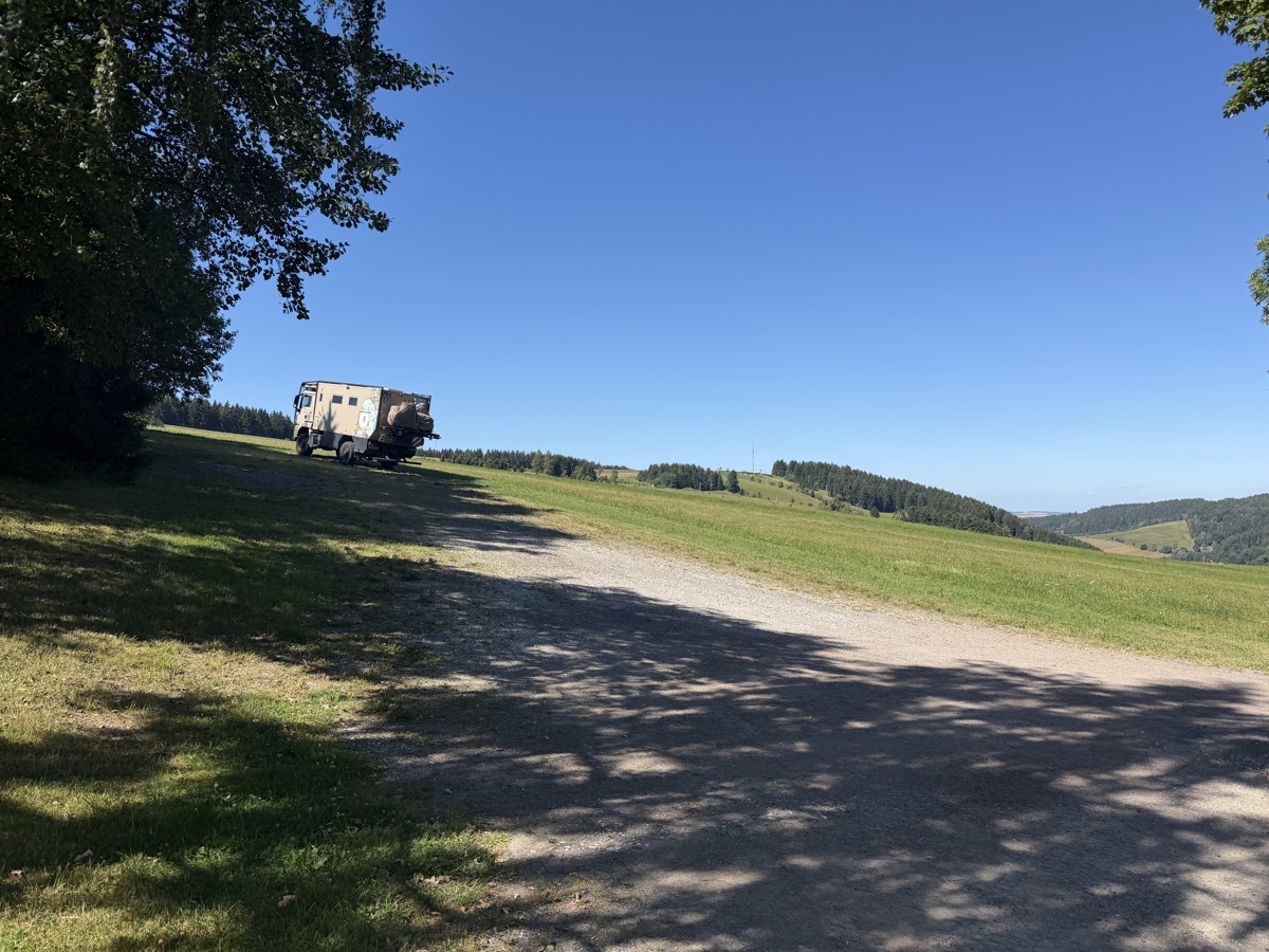 Mammothon steht auf einem geschotterten Weg an einem Hang, dahinter bewaldete Hügel