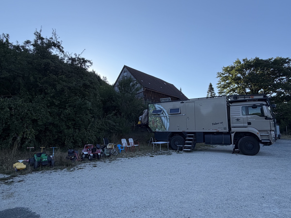 Mammothon steht auf Schotter vor einer Scheune, links eine Reihe Kinderfahrzeuge