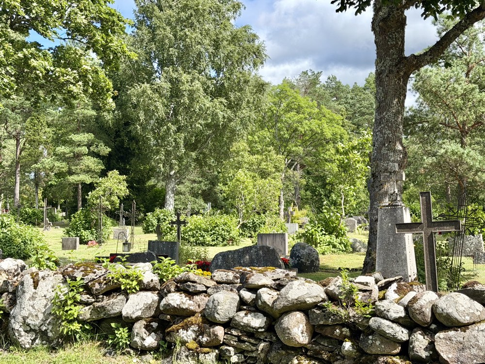 Alter Friedhof mit Steinmauer und Holzkreuzen zwischen hohen Bäumen
