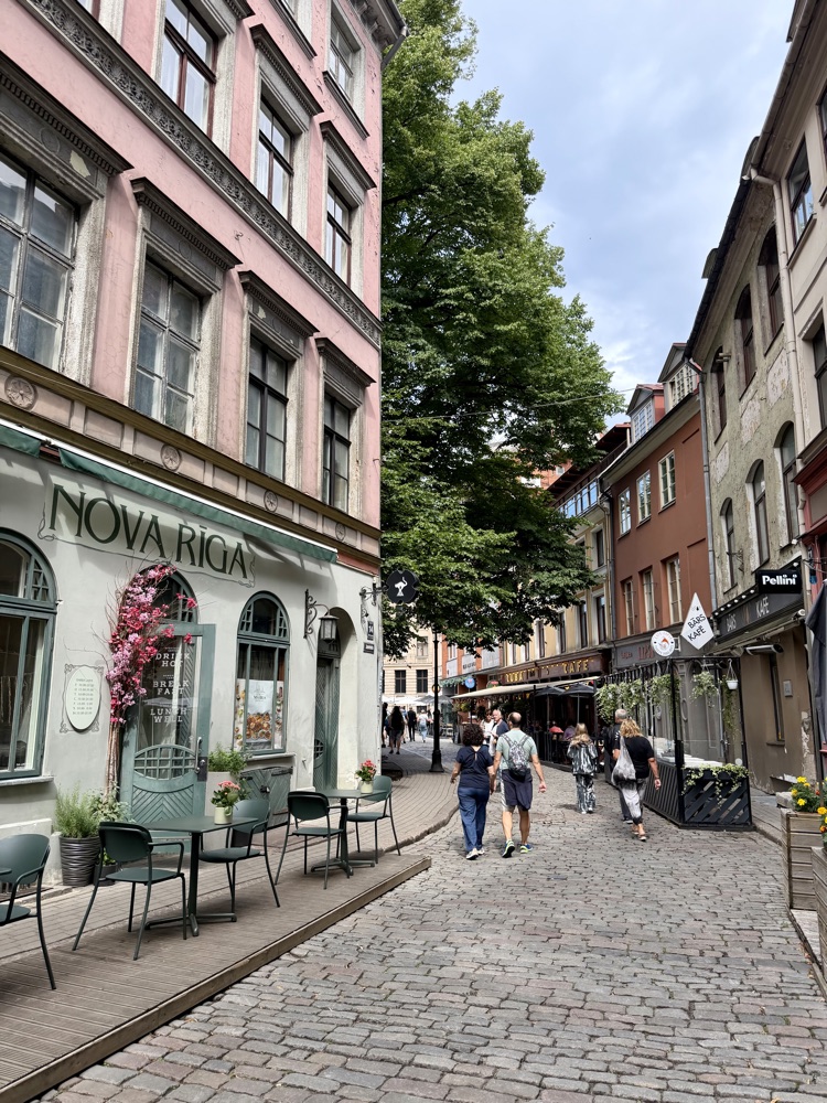 Gepflasterte Gasse mit bunten Häusern und einem Café in der Rigaer Altstadt
