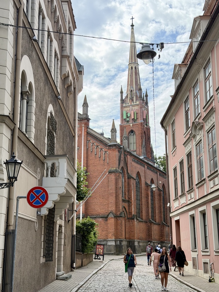 Schmale Gasse mit Blick auf eine rote Backsteinkirche mit spitzem Turm