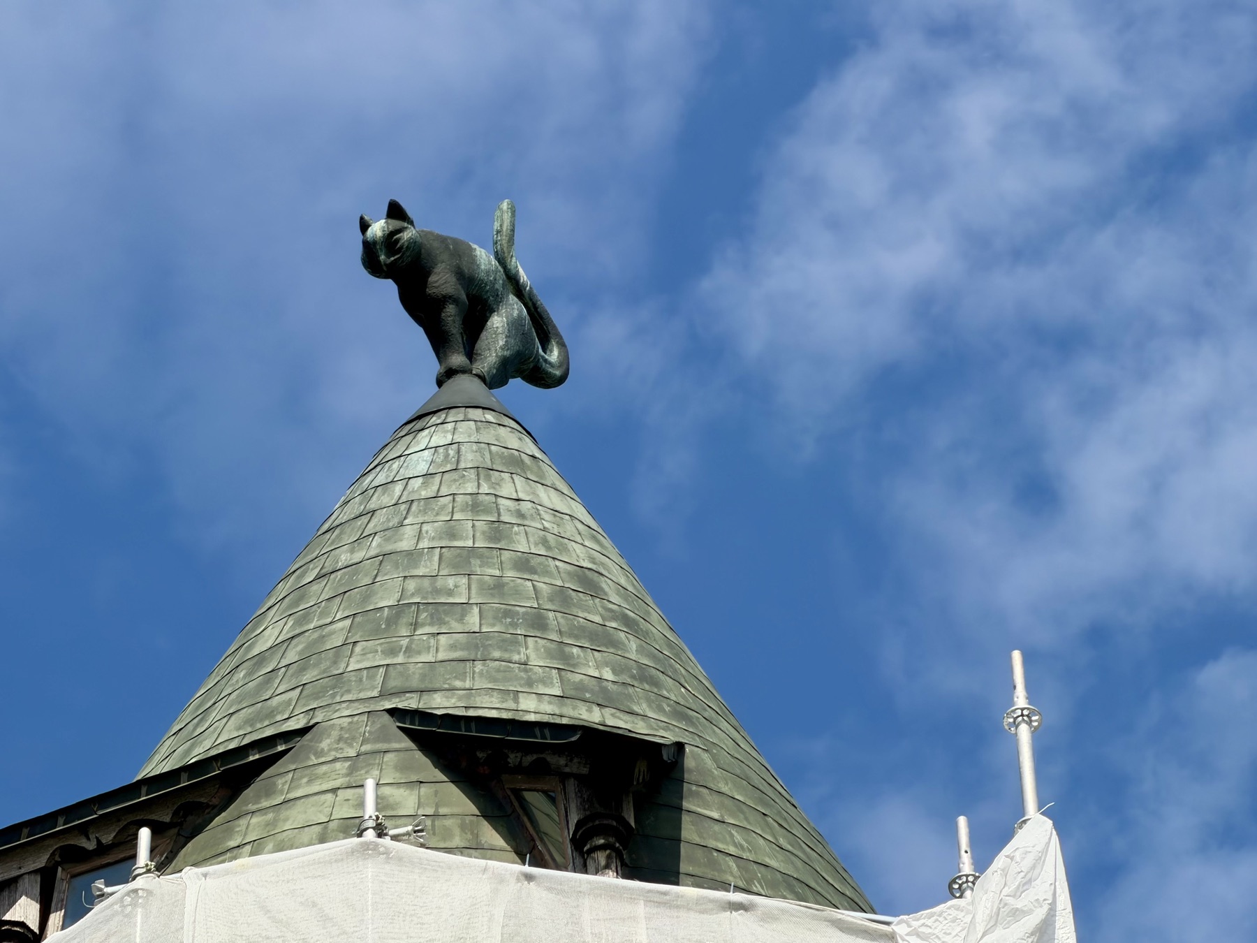 Katzenskulptur mit gekrümmtem Rücken auf einer grünen Turmspitze in Riga