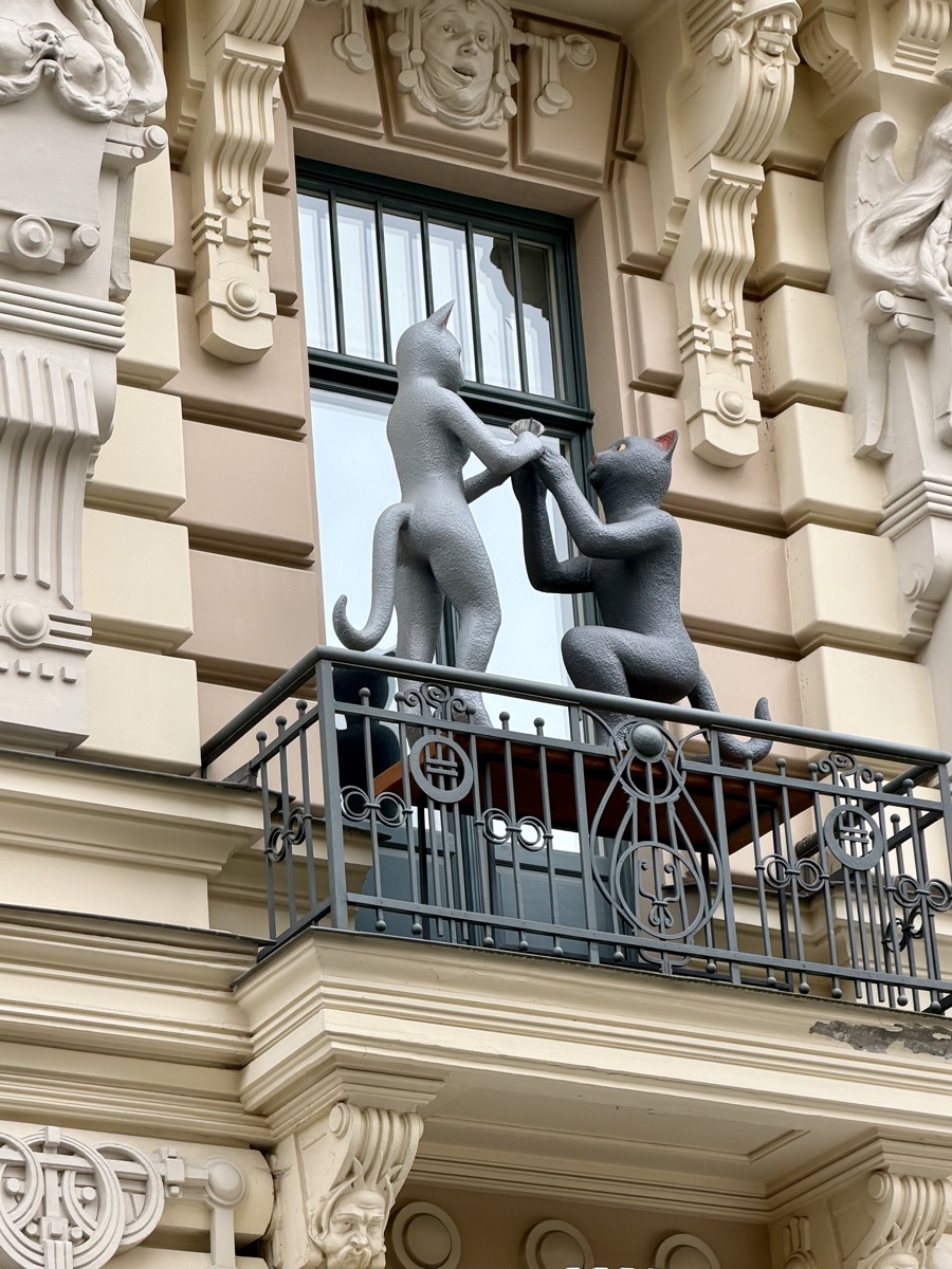 Zwei graue Katzenfiguren halten sich an den Pfoten auf einem Balkon