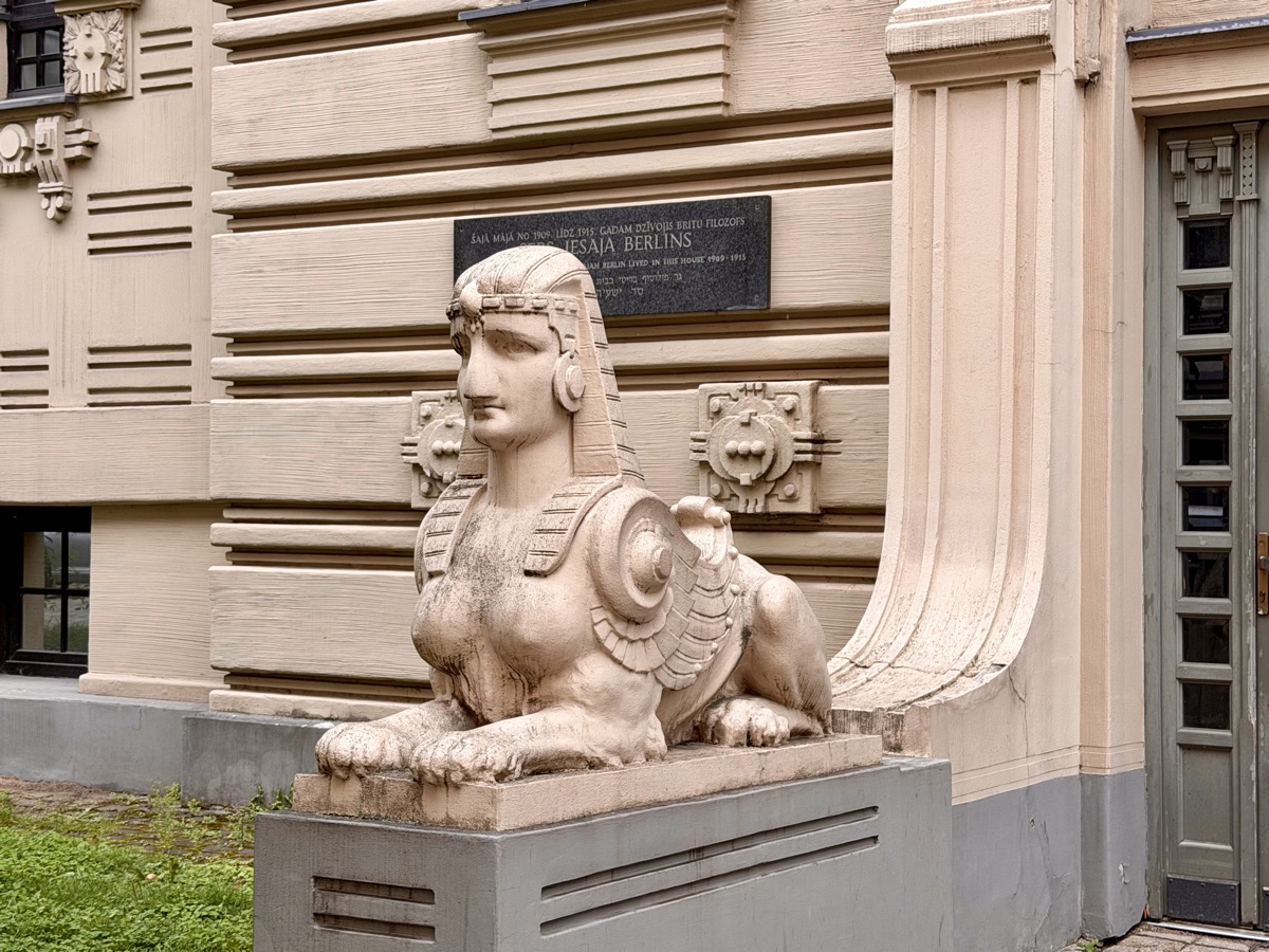 Steinerne Sphinx vor einer Hauswand mit Gedenktafel