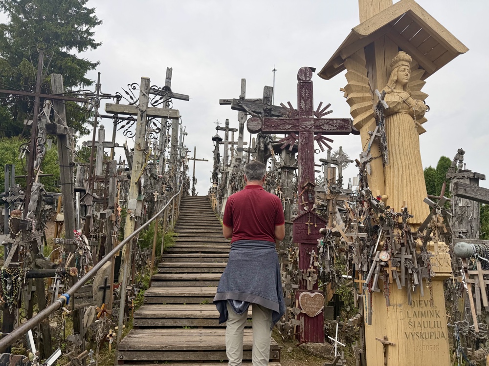 Sven steht auf einer Holztreppe zwischen Kreuzen, rechts eine Holzfigur mit Engel