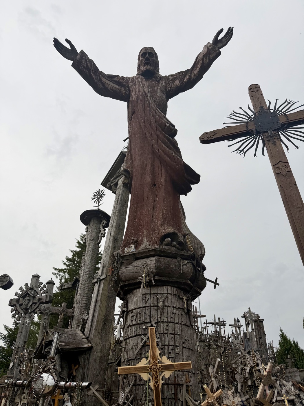 Große Christusfigur mit ausgebreiteten Armen auf einem Sockel, umgeben von Kreuzen