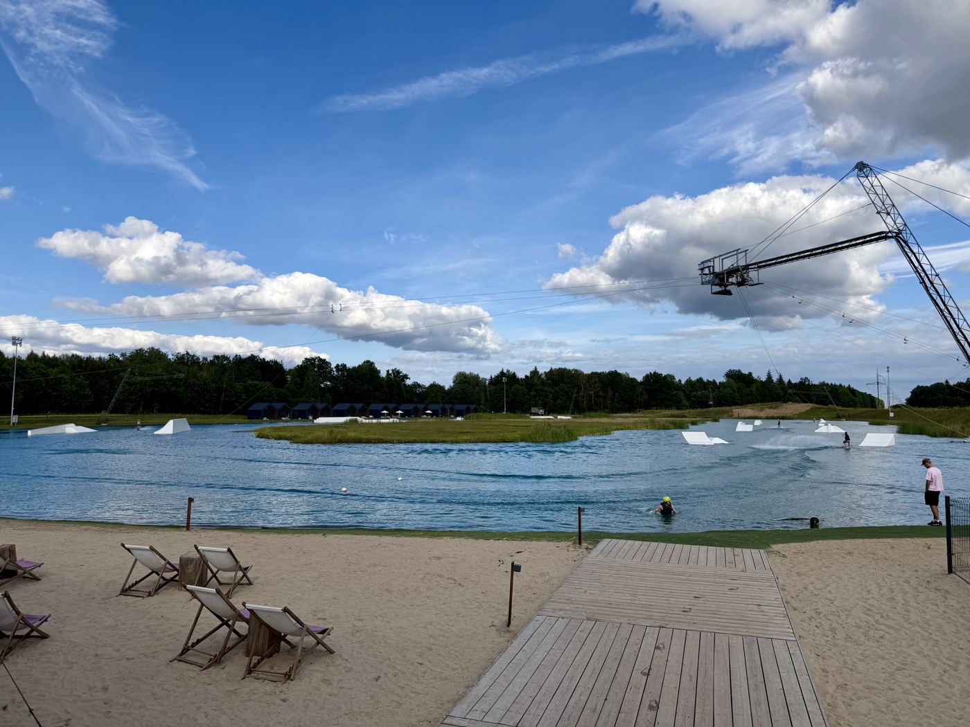 Wasserskianlage mit Strand, Liegestühlen und einem Steg unter blauem Himmel