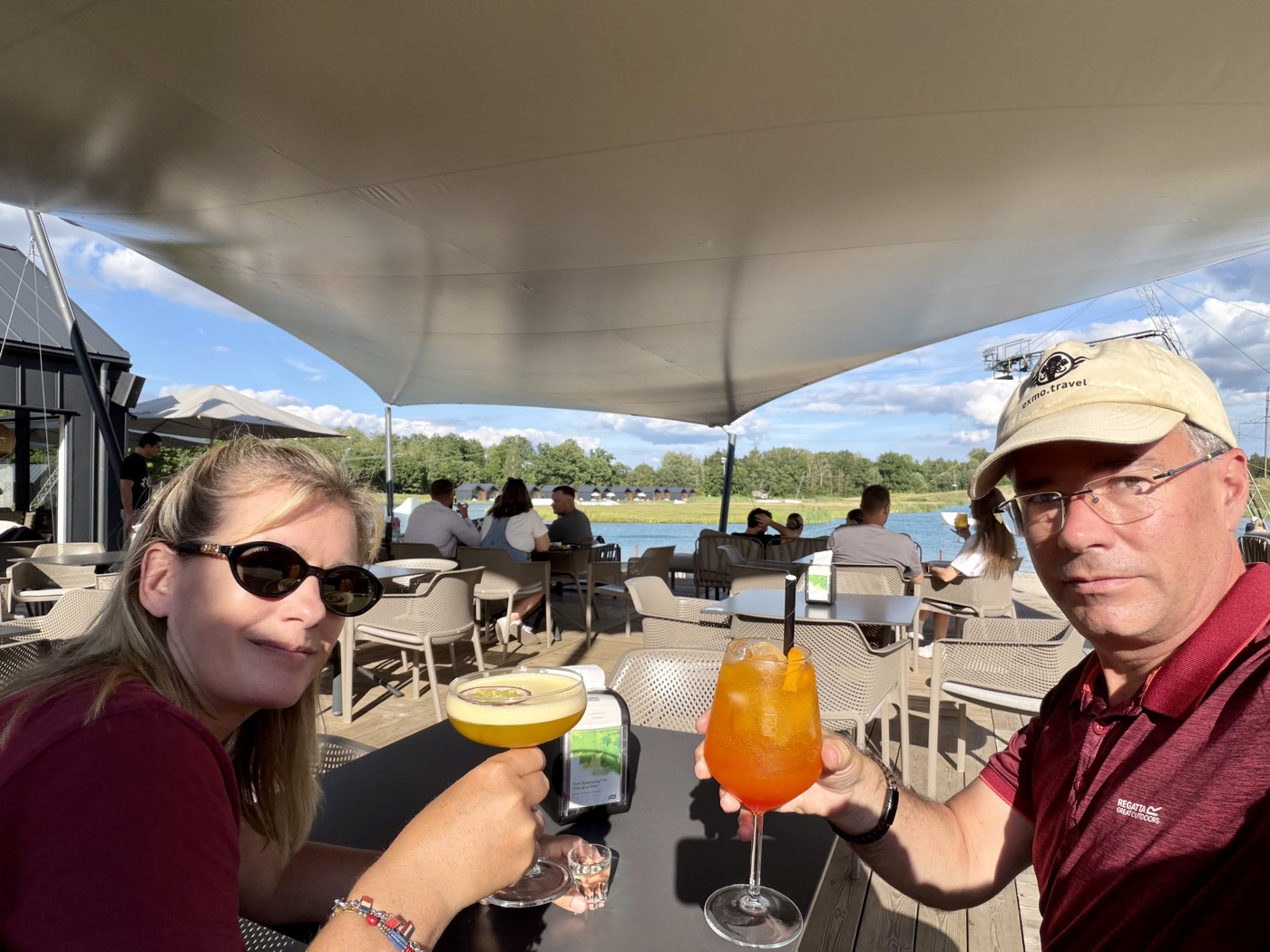 Sven und Saskia mit zwei Cocktails auf einer Terrasse mit Blick auf das Wasser