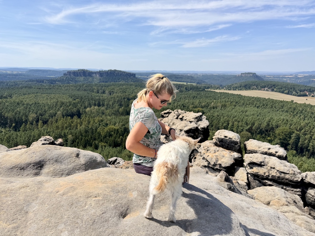 Saskia sitzt mit Lou auf einem Felsen vor einer weiten Waldlandschaft