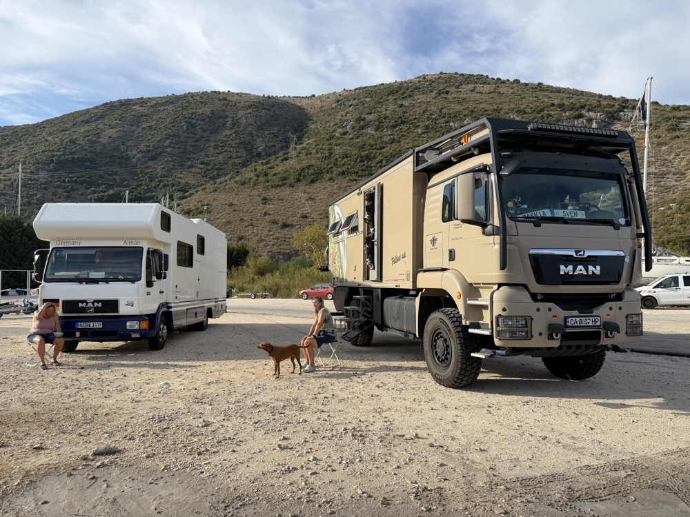 Das Mammothon neben einem weißen Fernreisemobil auf einem Kiesplatz am Meer, davor Lou an der Leine