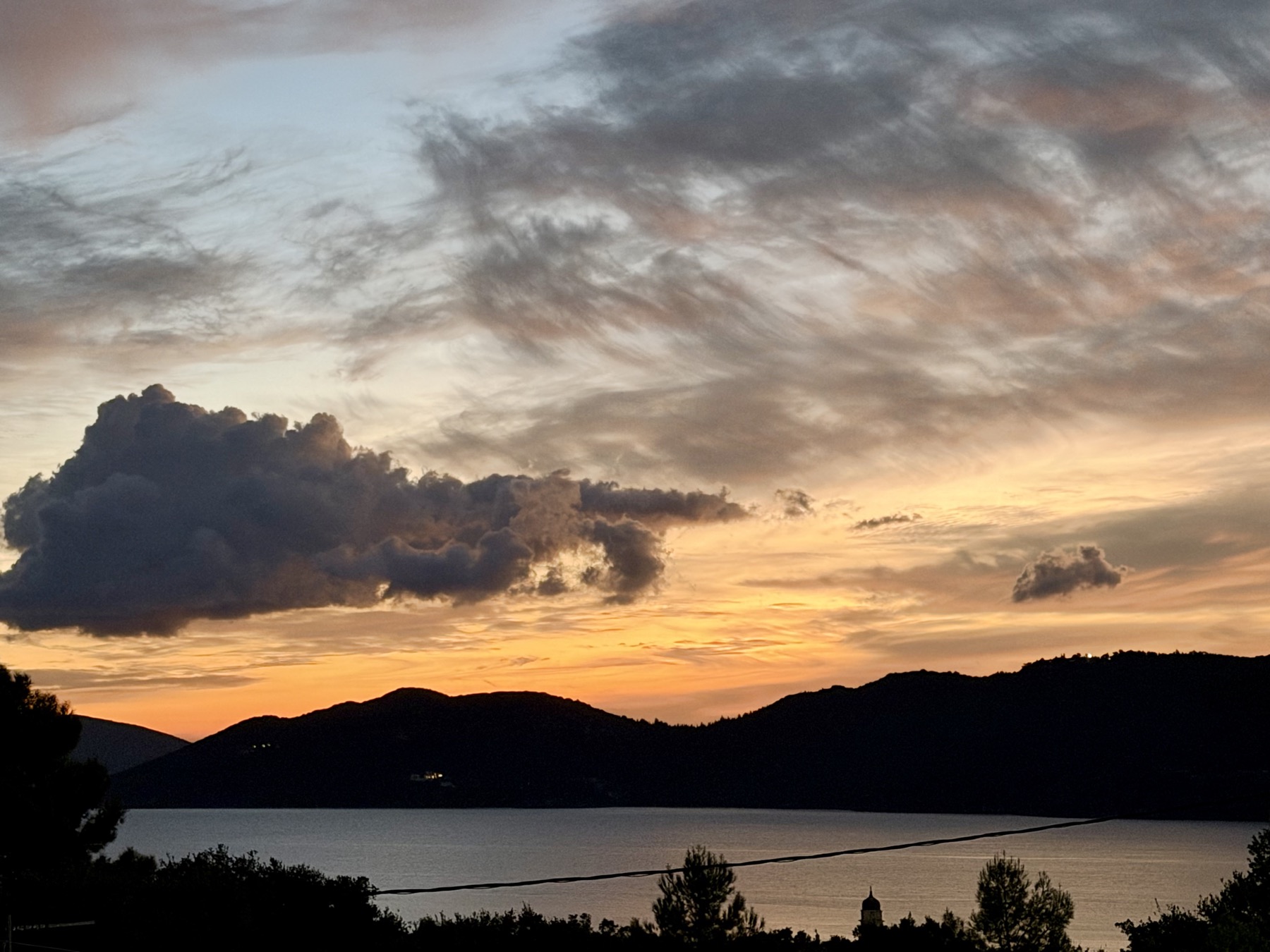 Sonnenuntergang mit dunklen Wolken über den Bergen und der Bucht von Sami
