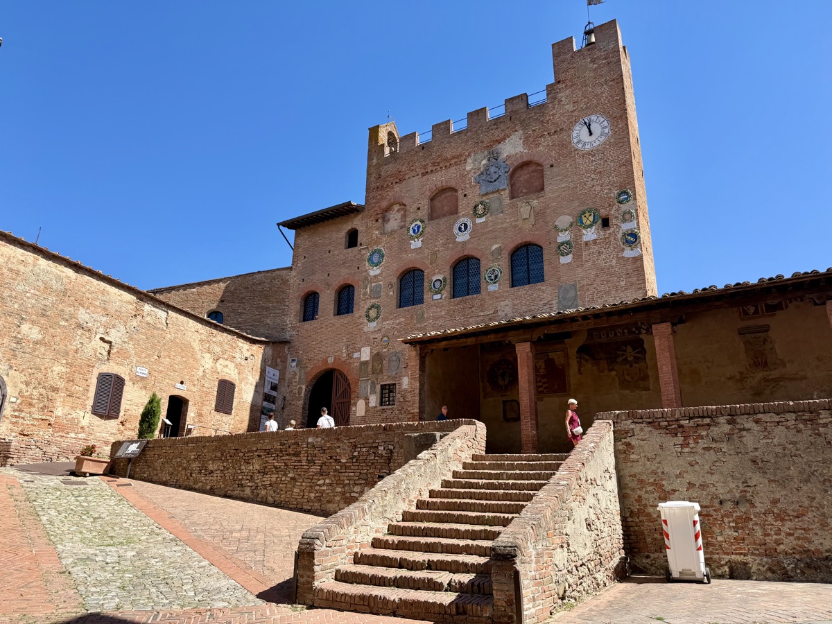Backsteinpalast mit Zinnen und Wappen an der Fassade, davor eine Freitreppe