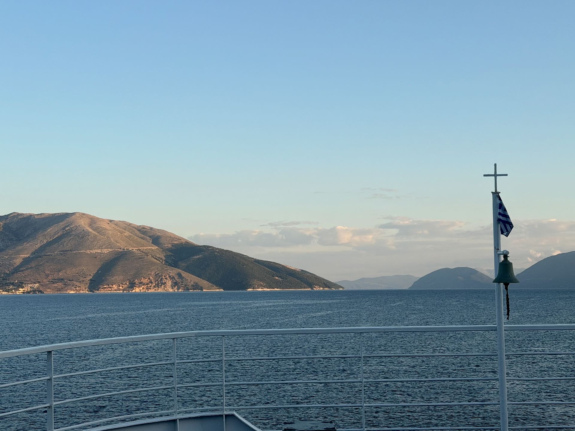 Blick vom Bug der Fähre mit griechischer Flagge auf Berge und das Meer