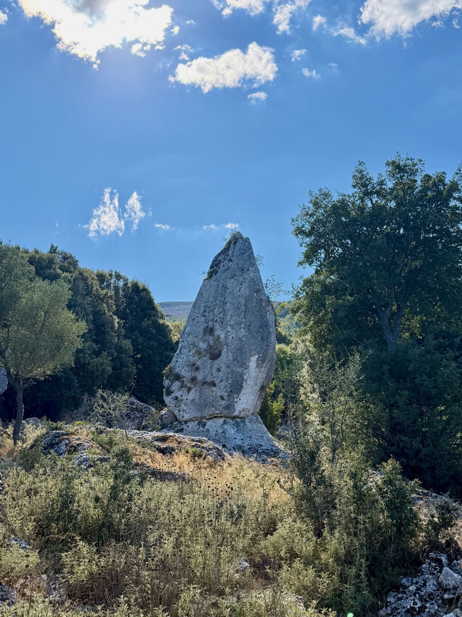 Heller Steinmonolith zwischen Büschen und Bäumen unter blauem Himmel