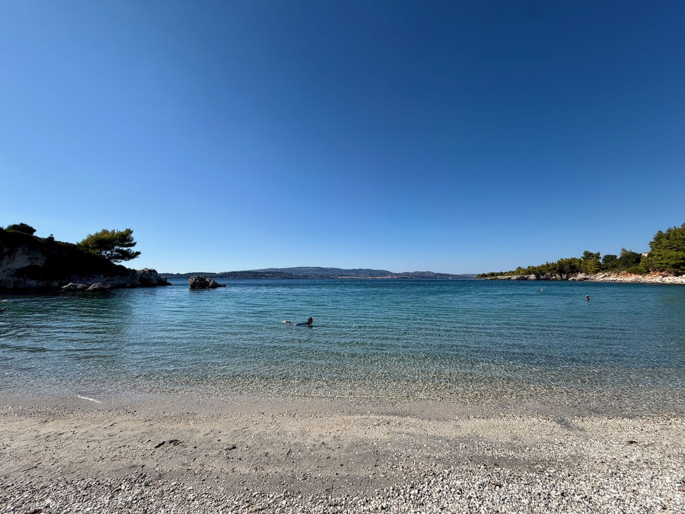 Ruhige Bucht mit hellem Strand und klarem Wasser, im Hintergrund bewaldete Landzungen