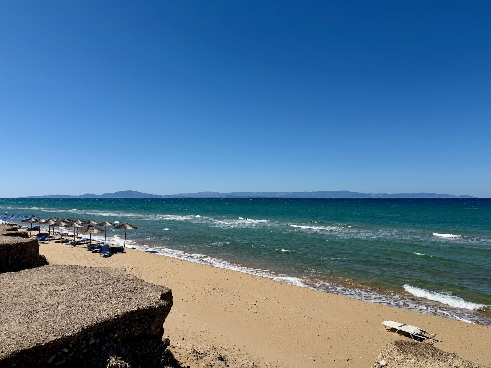 Sandstrand mit Wellen und Sonnenschirmen unter blauem Himmel