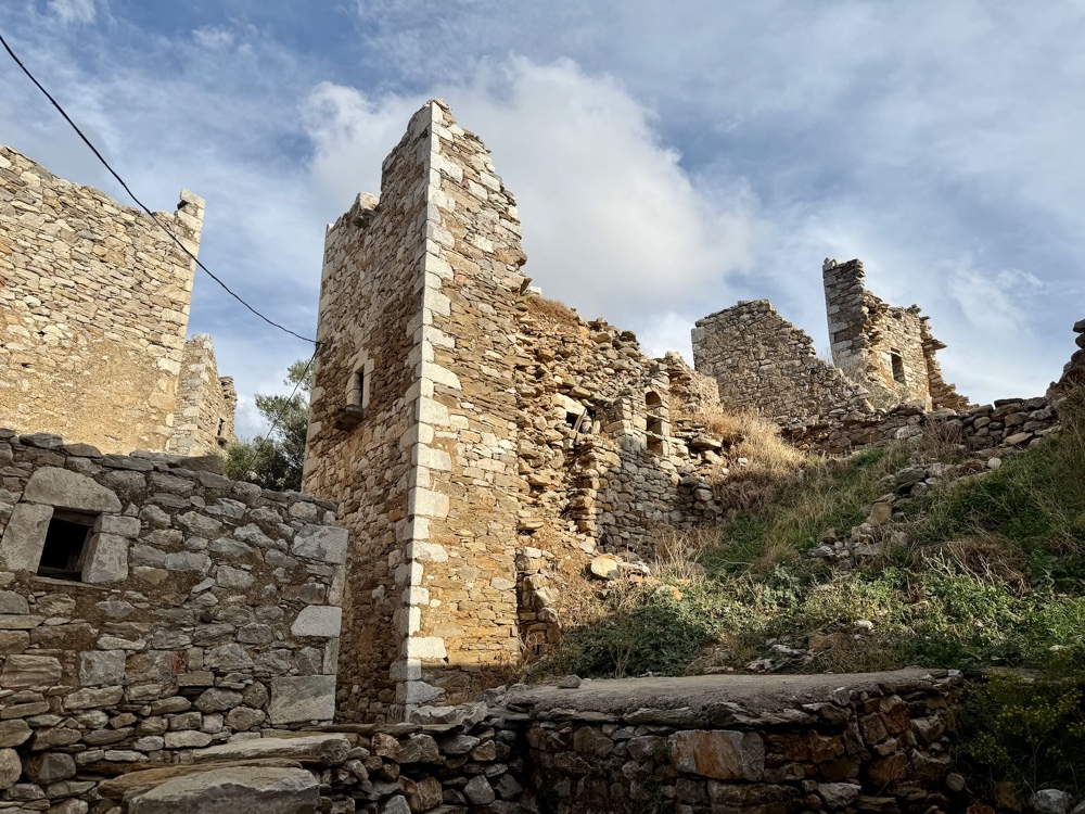 Ein hoher, verfallener Turm aus Stein zwischen Mauerresten unter blauem Himmel